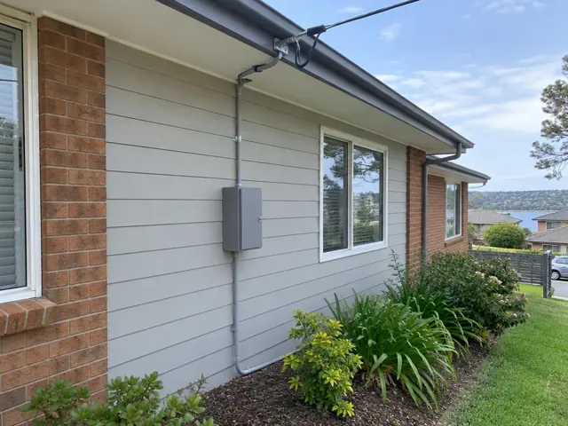 Overhead service cable and bracket on a weatherboard house with meter box and garden in Point Clare