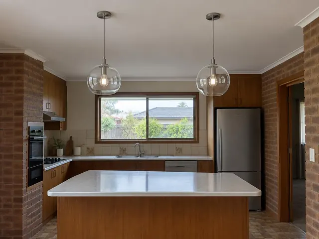 Two pendant lights over a kitchen island in a brick-walled home in Umina Beach
