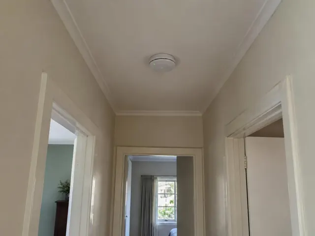 Ceiling smoke alarm in a narrow hallway with doorways and crown molding in Woy Woy